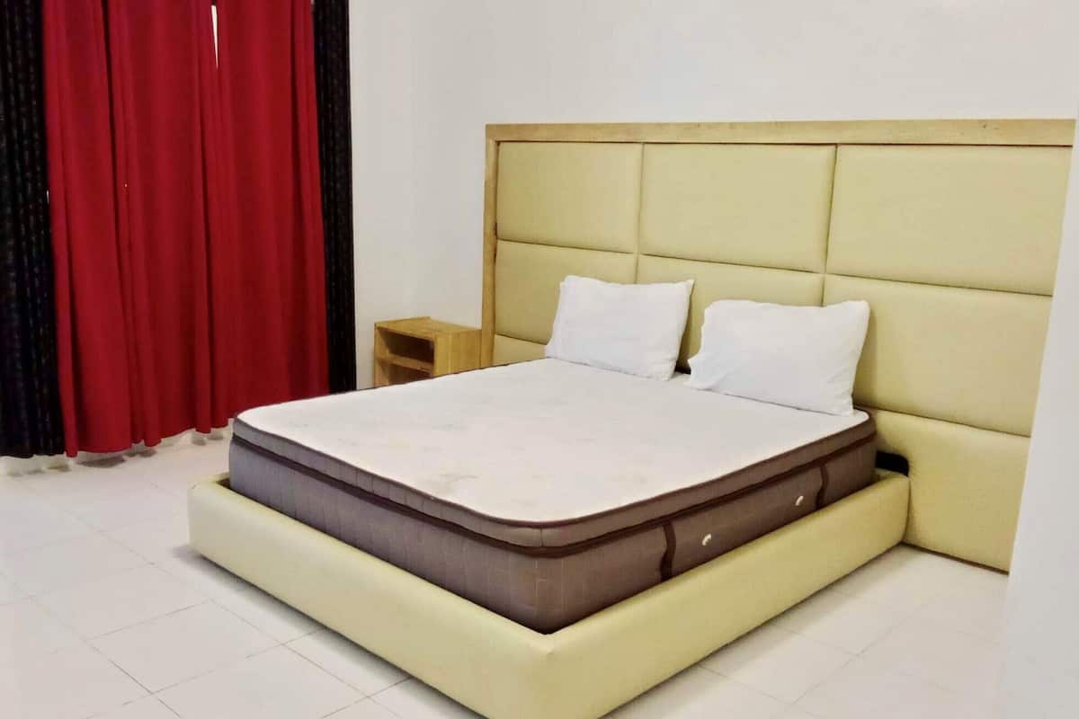 A bed with a headboard, a nightstand, and a red curtain.