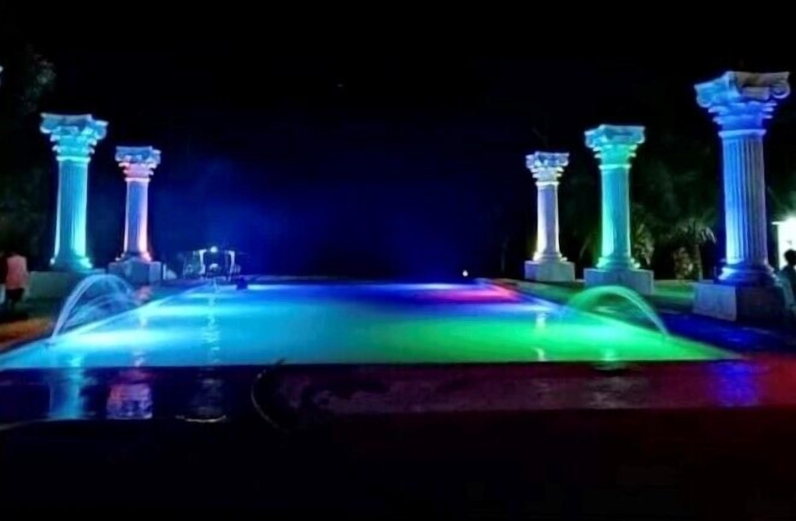 A nighttime view of a fountain with illuminated columns and a water feature.