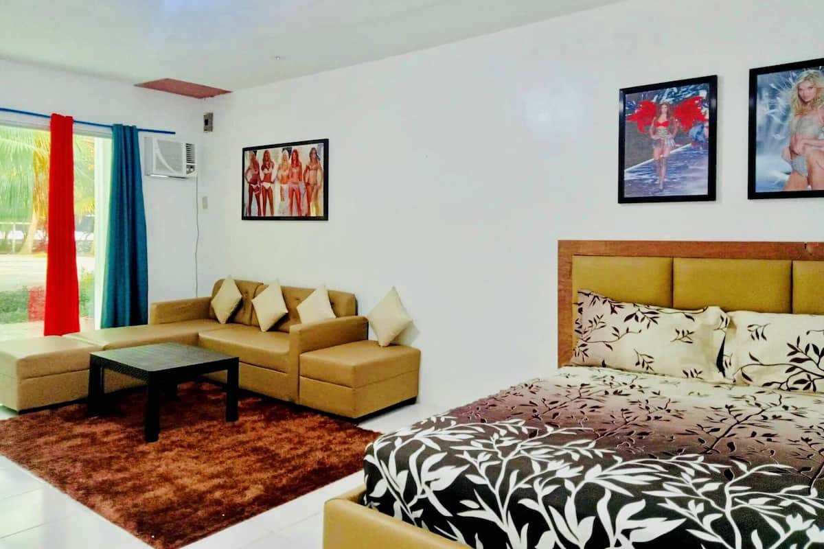 A modern living room with a sofa, a coffee table, and a bed with a patterned headboard. There are two framed pictures on the wall.