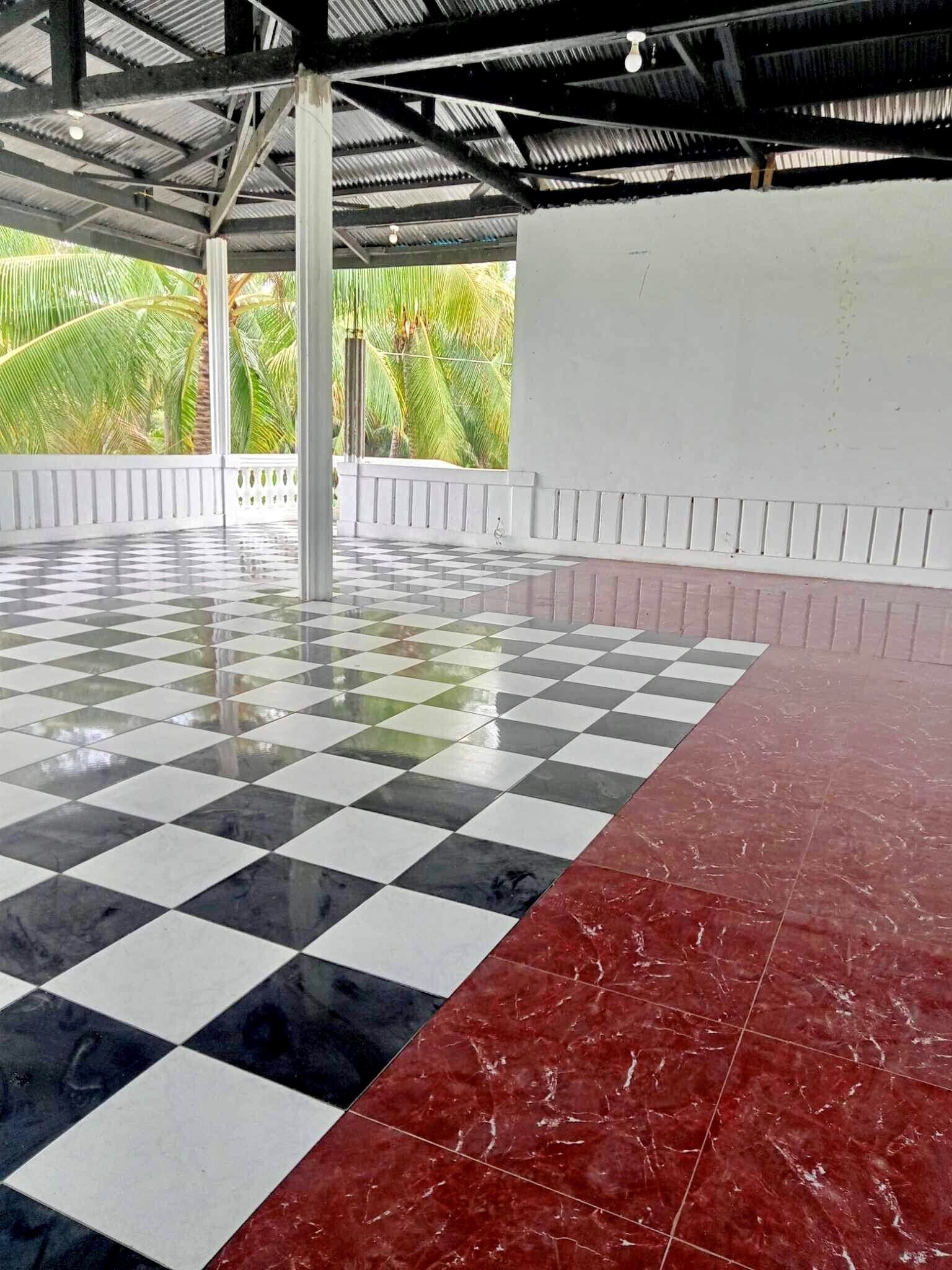 An indoor pool area with a checkered floor, a red section, and a view of palm trees outside.