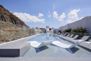 A swimming pool with lounge chairs, a rocky hillside, and a clear sky.