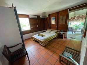 Une pièce comprenant un lit, une chaise, une petite table, un luminaire suspendu et donnant sur l’extérieur.