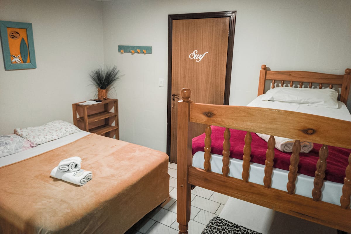 Un dormitorio con dos camas, un cabecero de madera, una mesita de noche de madera con una planta y una puerta con la leyenda 'Surf'.