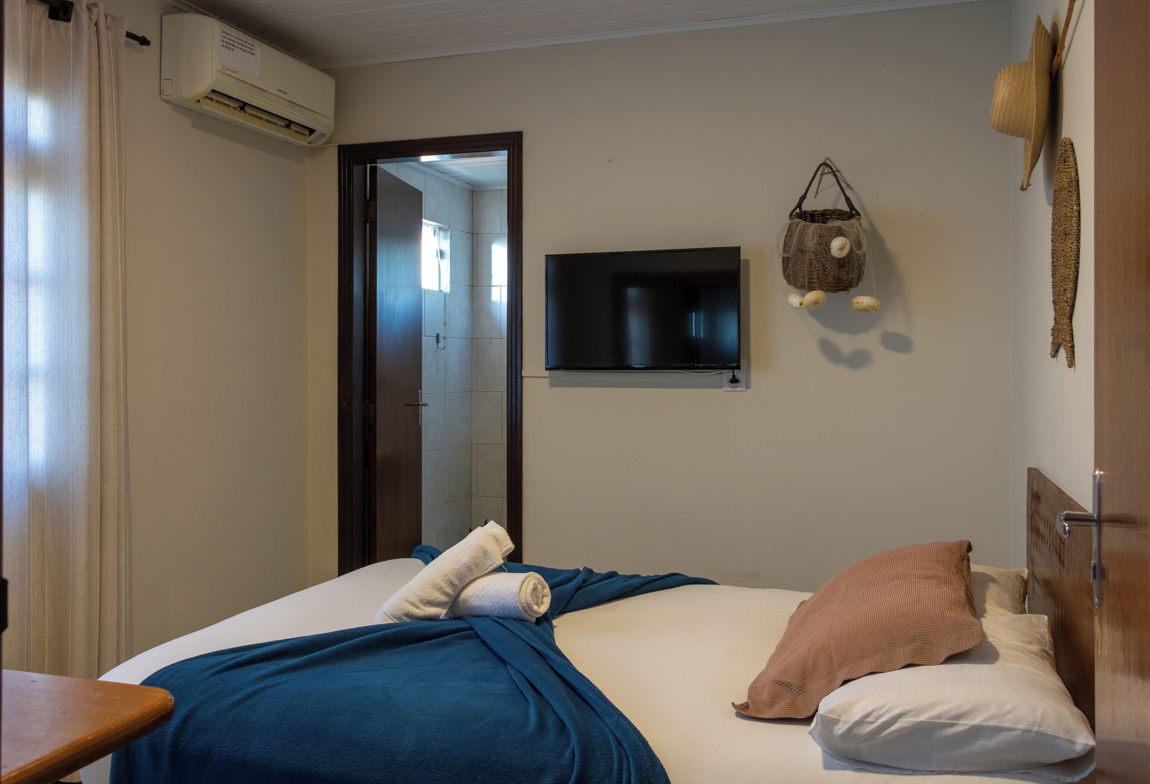 Una habitación de hotel con una cama, un televisor montado en la pared y un equipo de aire acondicionado.