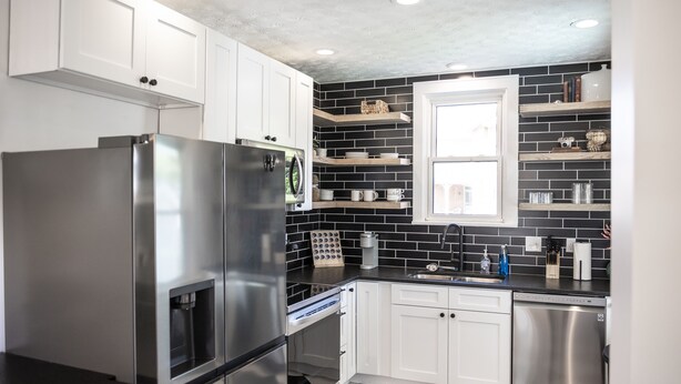 A modern kitchen with white cabinets, black and white checkered flooring, stainless steel appliances, and black brick backsplash. - 3 BR cozy + renovated walkable downtown stay (Hilliard)