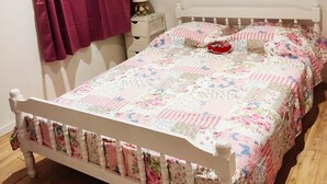 Ein Schlafzimmer mit einem weißen Bett, blumigem Bettzeug, einem roten Gegenstand auf dem Bett, einem Nachttisch mit einer Lampe und einem Löwenbild an der Wand.