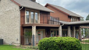 Une maison à deux étages avec une façade en pierre, un balcon doté d’une balustrade en métal et une pelouse bien entretenue.
