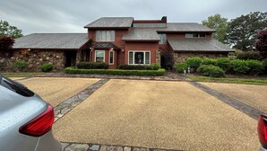 Une maison à deux étages avec une façade en pierre, une allée en pierre et une voiture garée au premier plan.
