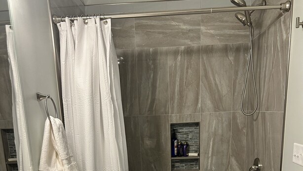 Une salle de bain avec un lavabo blanc, une baignoire, une douche dotée d’une porte en verre et un porte-serviettes.