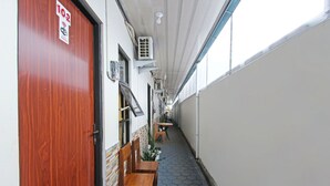 Un couloir étroit avec une porte en bois portant l’inscription « 102 », des unités de climatisation et un espace détente avec des chaises et une table.