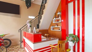 Un comptoir d’accueil aux couleurs rouge et blanc, un escalier, une chaise en bois, une plante en pot et une moto.