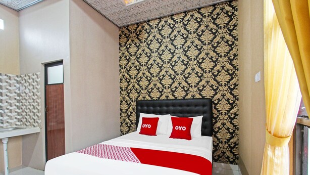 Une chambre d’hôtel avec un lit, deux oreillers rouges, un papier peint à motifs et une fenêtre avec des rideaux.