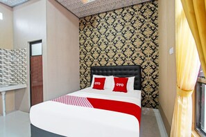 Ein Hotelzimmer mit einem Bett, zwei roten Kissen, Tapete mit Muster und einem Fenster mit Vorhängen.