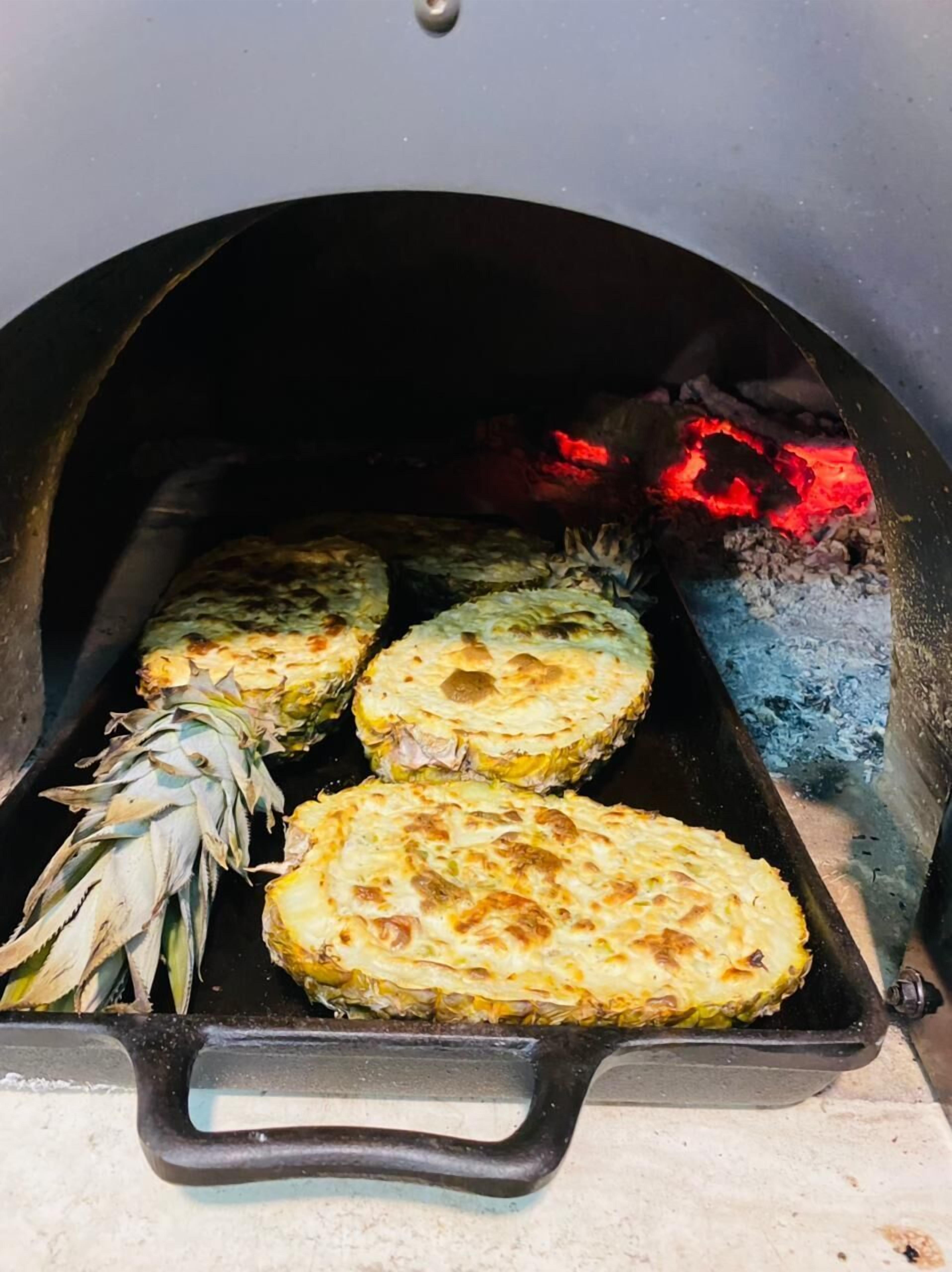 A grill with four pineapple halves and a whole pineapple inside.