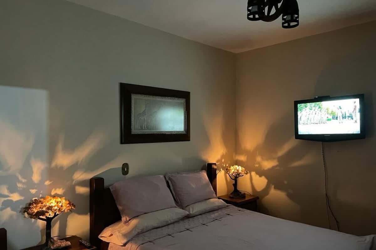 Een slaapkamer met een bed, twee nachtkastjes met lampen, een wandtelevisie en een ingelijste foto.
