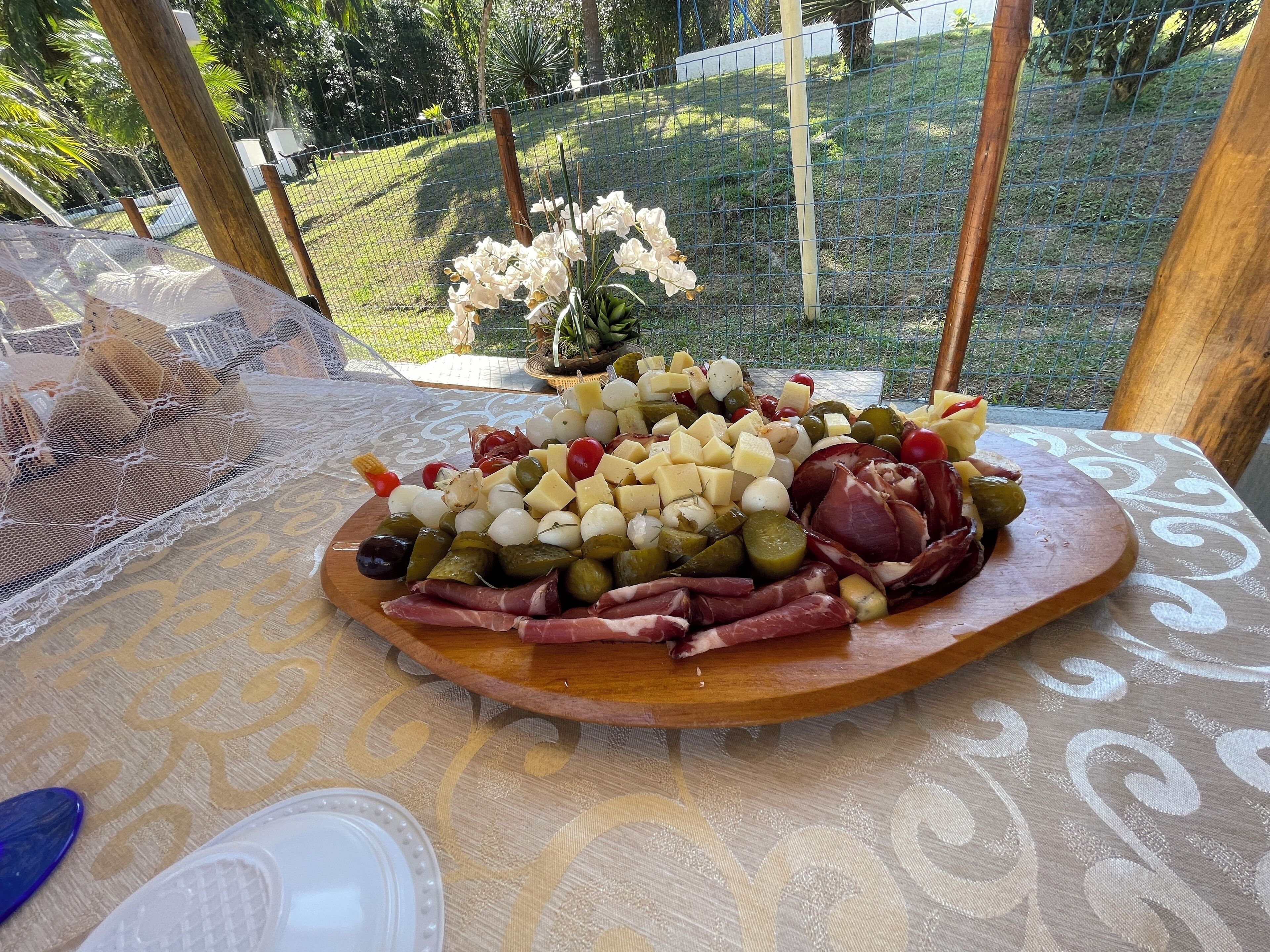 A charcuterie board with various cheeses, meats, and olives on a wooden board, placed on a table with a lace tablecloth.