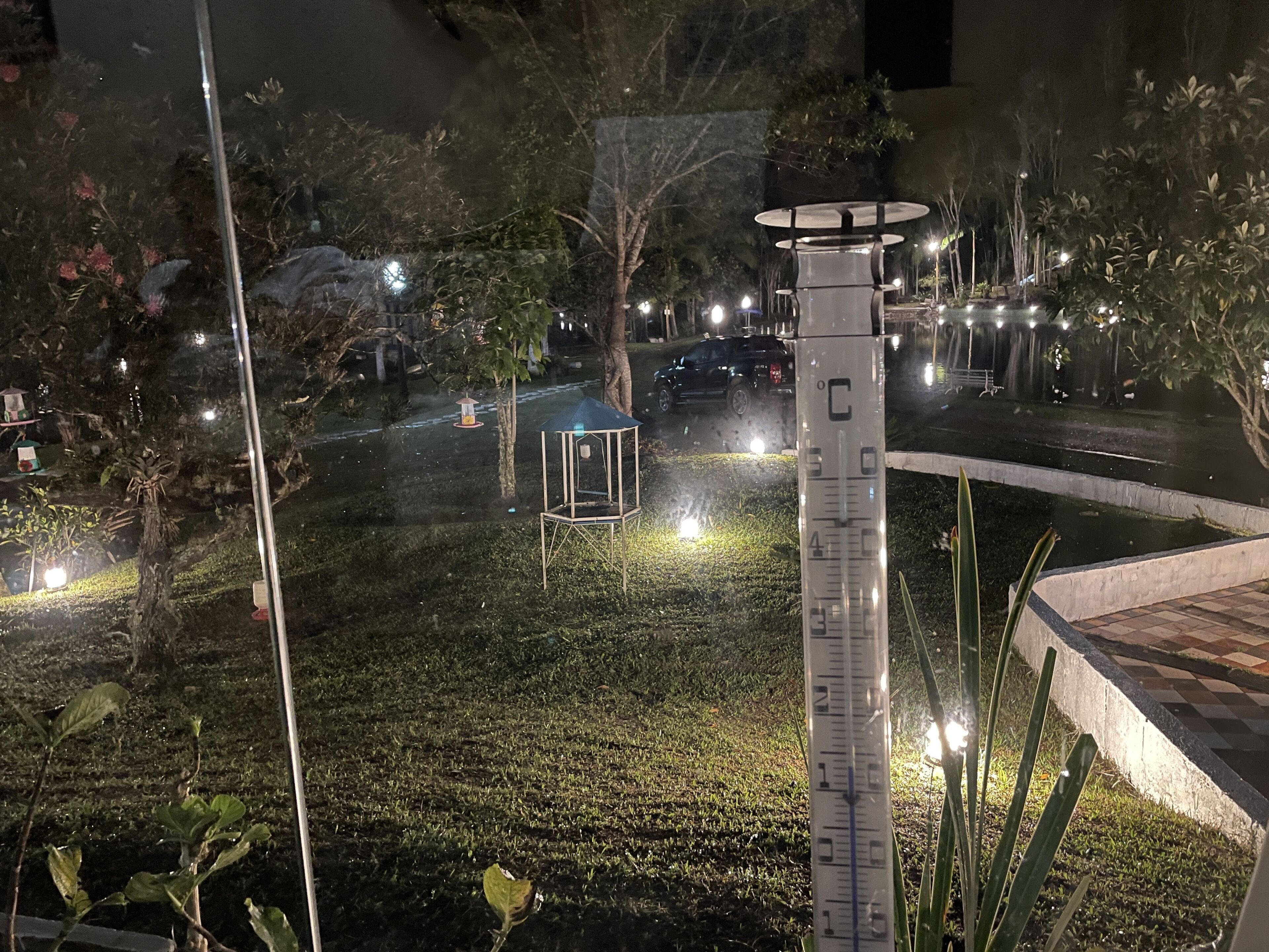 A nighttime view of a park with a thermometer, trees, and a gazebo.