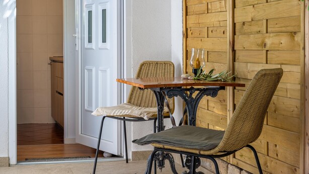 Eine Sitzecke mit einem Holztisch und zwei Korbstühlen, eine weiße Tür und eine Holzwand.