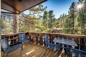 Una terraza de madera con sillas y mesas de metal, con vistas a una zona boscosa.
