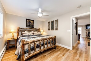 Un dormitorio con un armazón de cama de madera rústica, ventilador de techo y vista a un pasillo con chimenea.