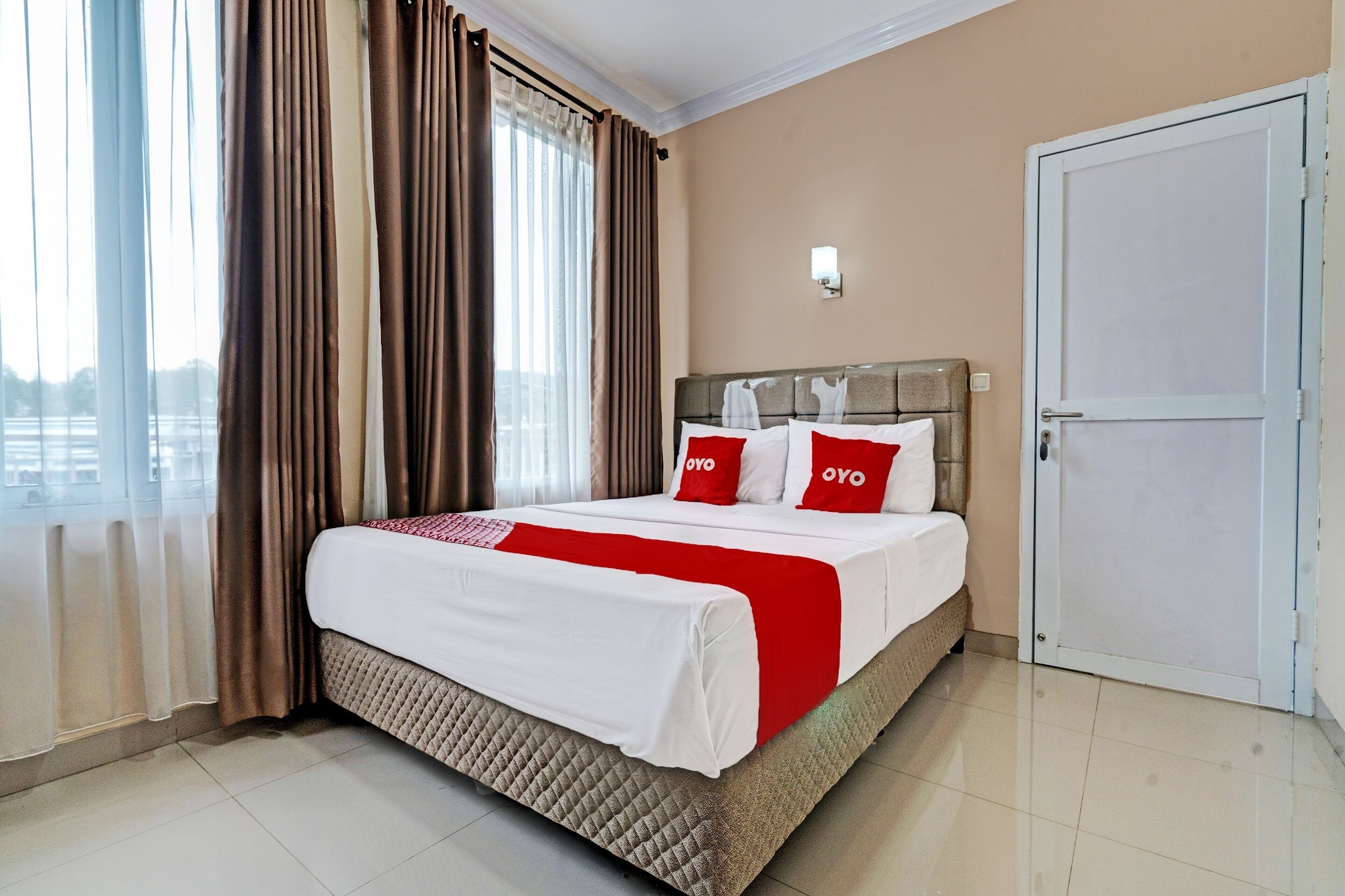 A hotel room with a bed, curtains, a door, and a window.
