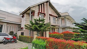 A modern two-story building with a balcony, surrounded by well-maintained gardens and a parked motorcycle. - OYO 92023 Singgasana Cipelah Syariah (Tjikadjang)