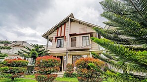 A two-story house with a balcony, surrounded by well-maintained gardens and tropical plants. - OYO 92023 Singgasana Cipelah Syariah (Tjikadjang)