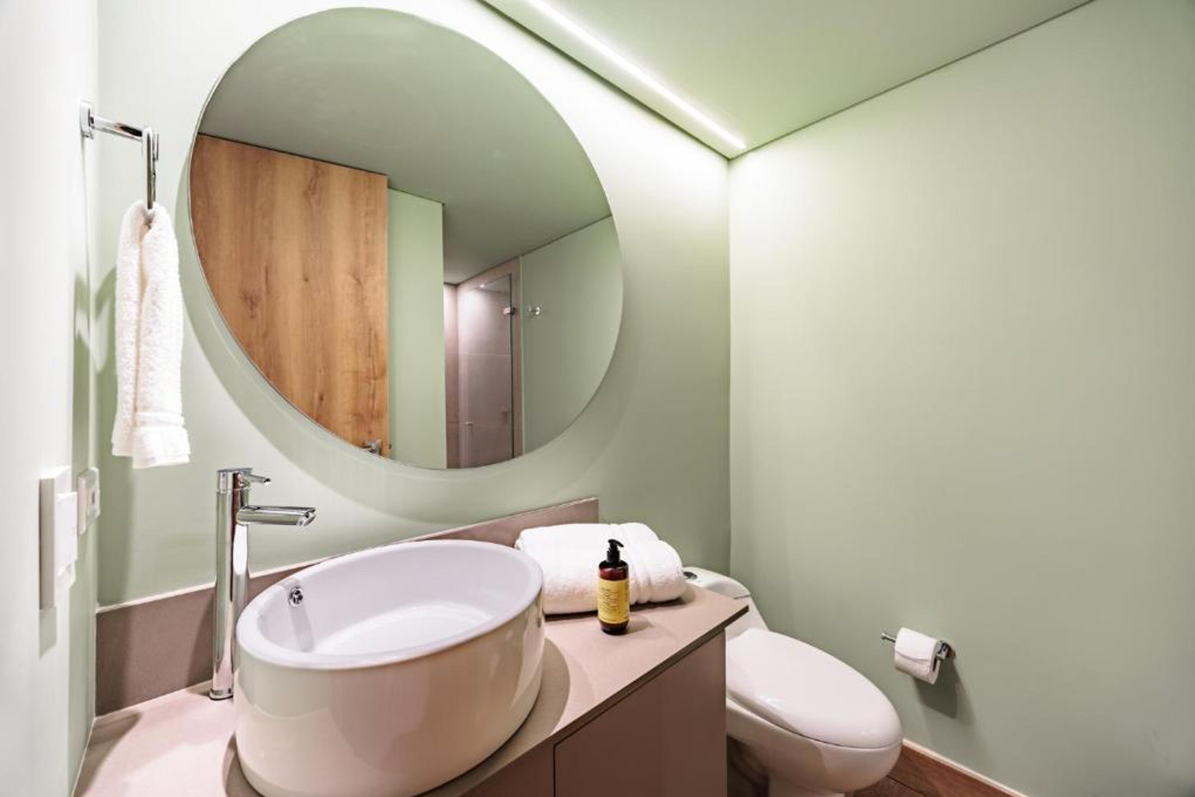 A bathroom with a round mirror, a sink, and a toilet.
