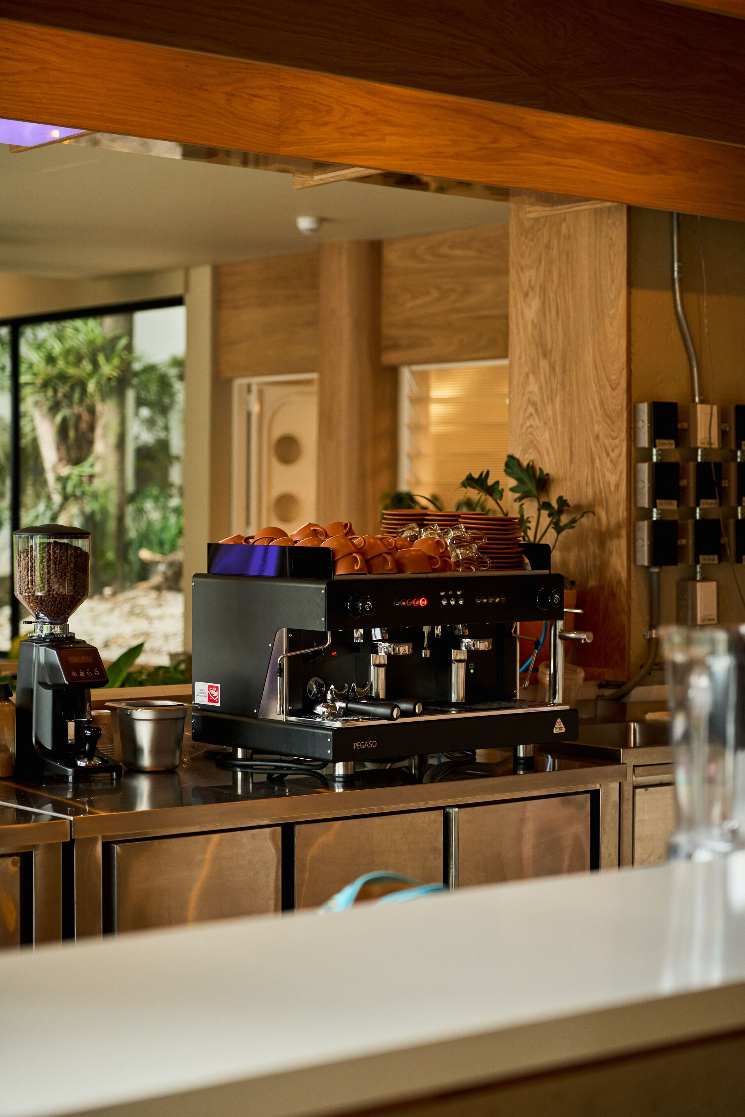 A coffee machine with a grinder, a stack of cups, and a small pot on a counter.