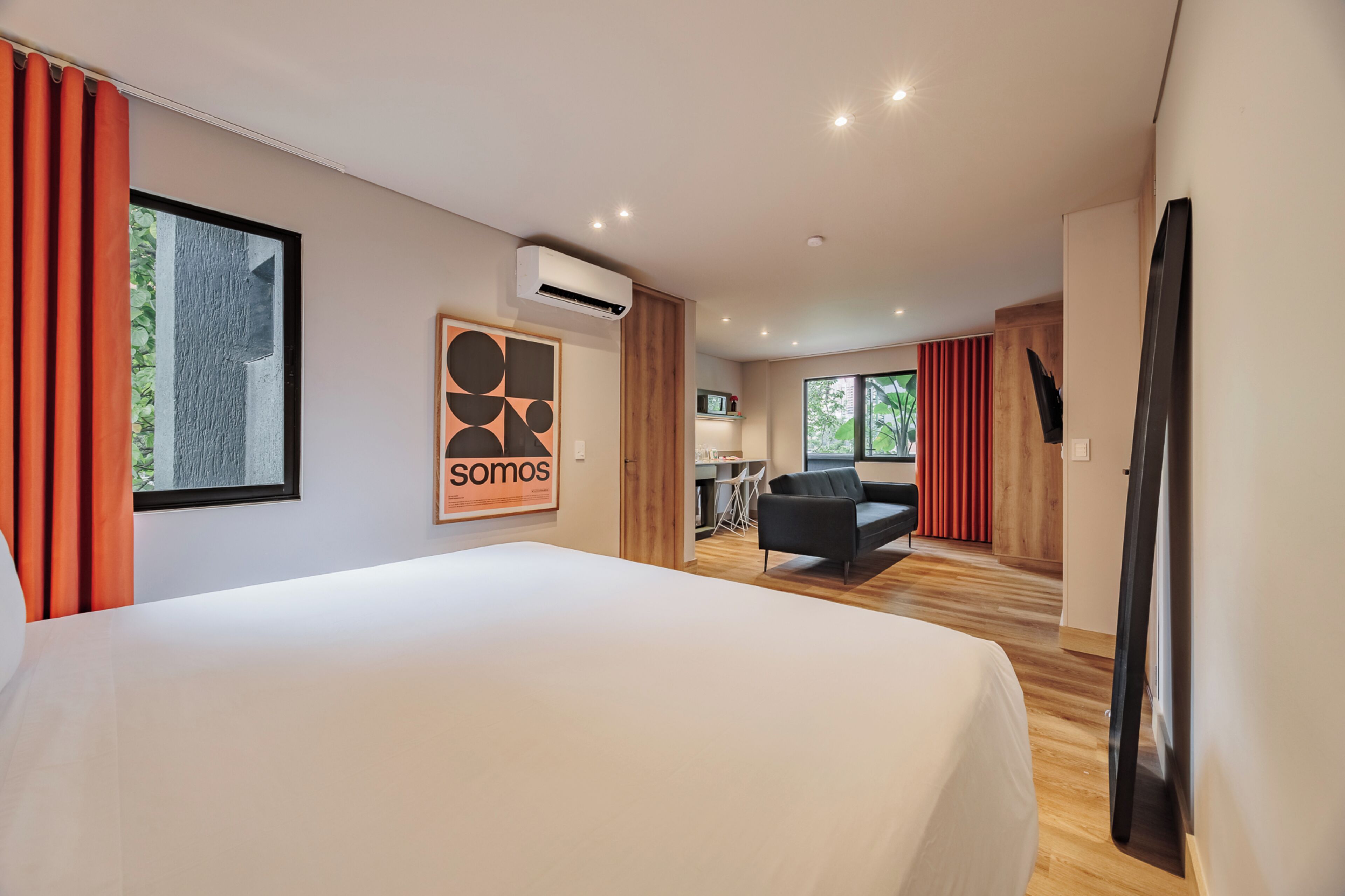 A modern hotel room with a large bed, a desk with a chair, a sofa, and a TV.