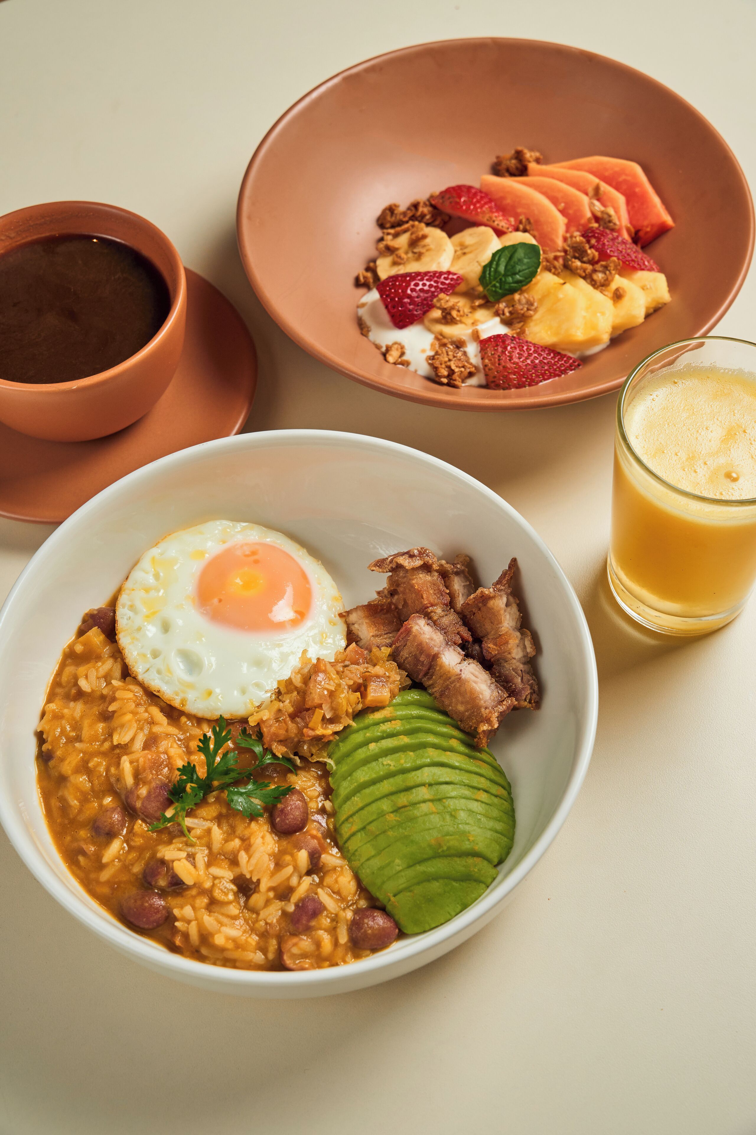 A table with three bowls of food, a cup of coffee, and a glass of orange juice.