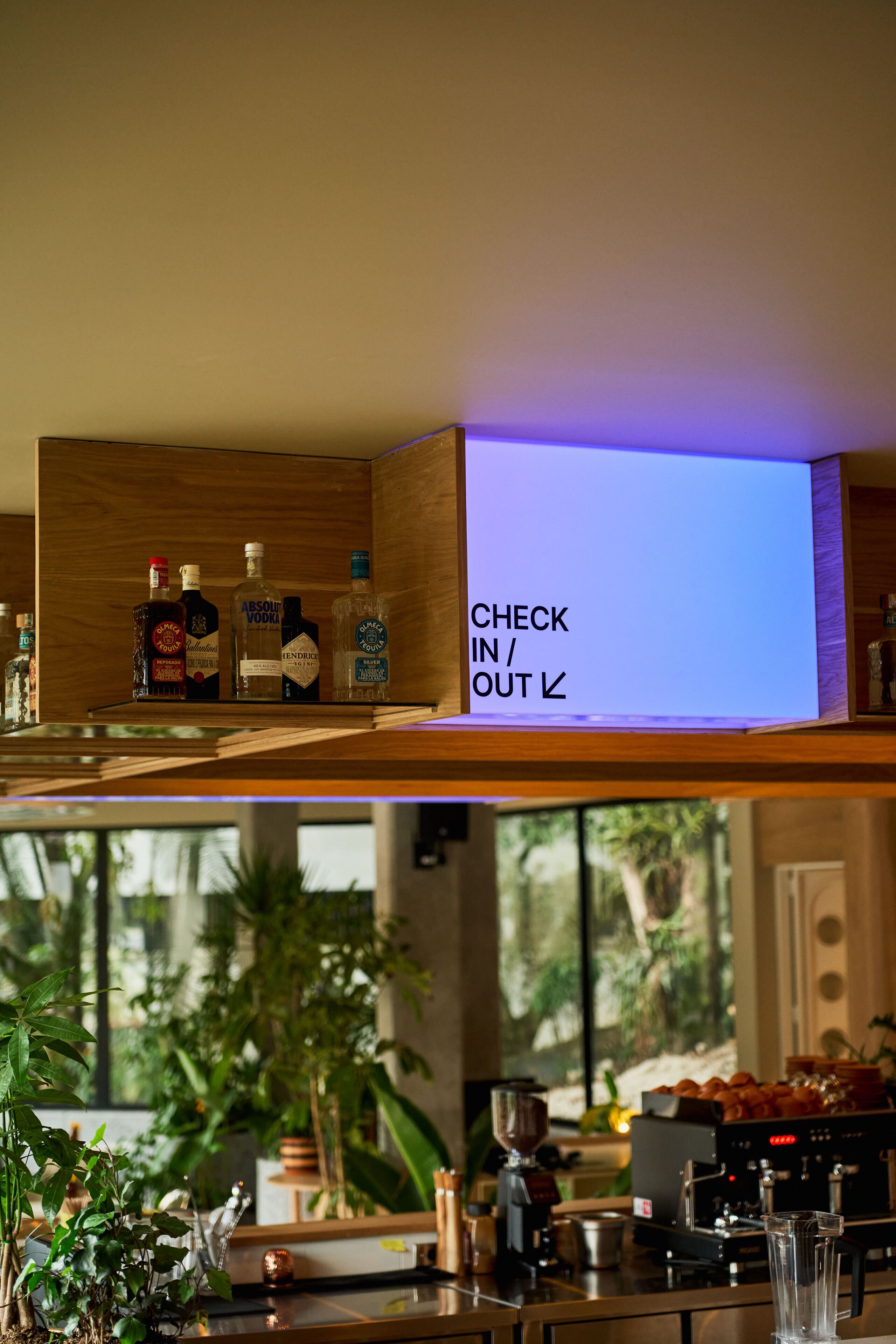 A bar area with a check-in/out sign, bottles of liquor, and a coffee machine.