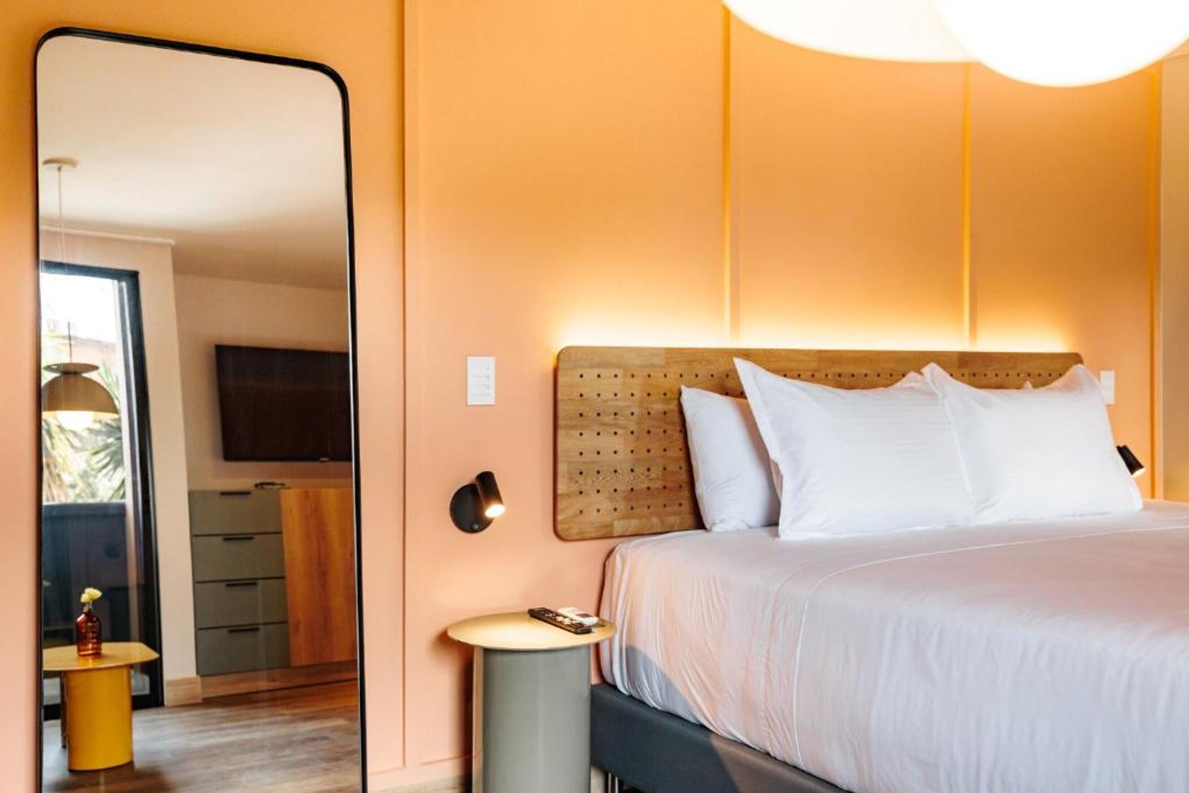 A bedroom with a large mirror, a wooden headboard, a bedside table, and a TV mounted on the wall.