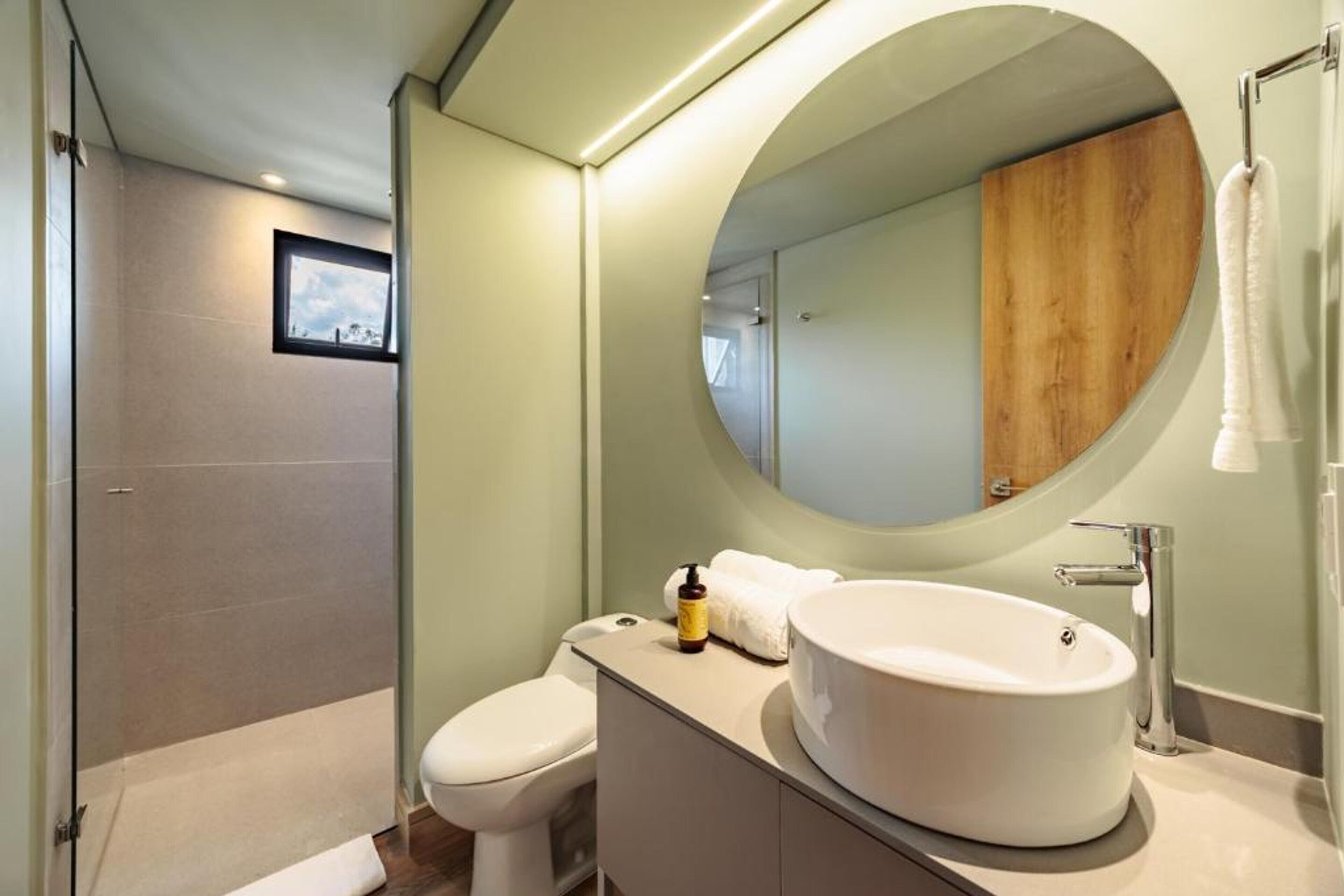 Un baño moderno con un espejo redondo, un lavabo blanco y un inodoro.