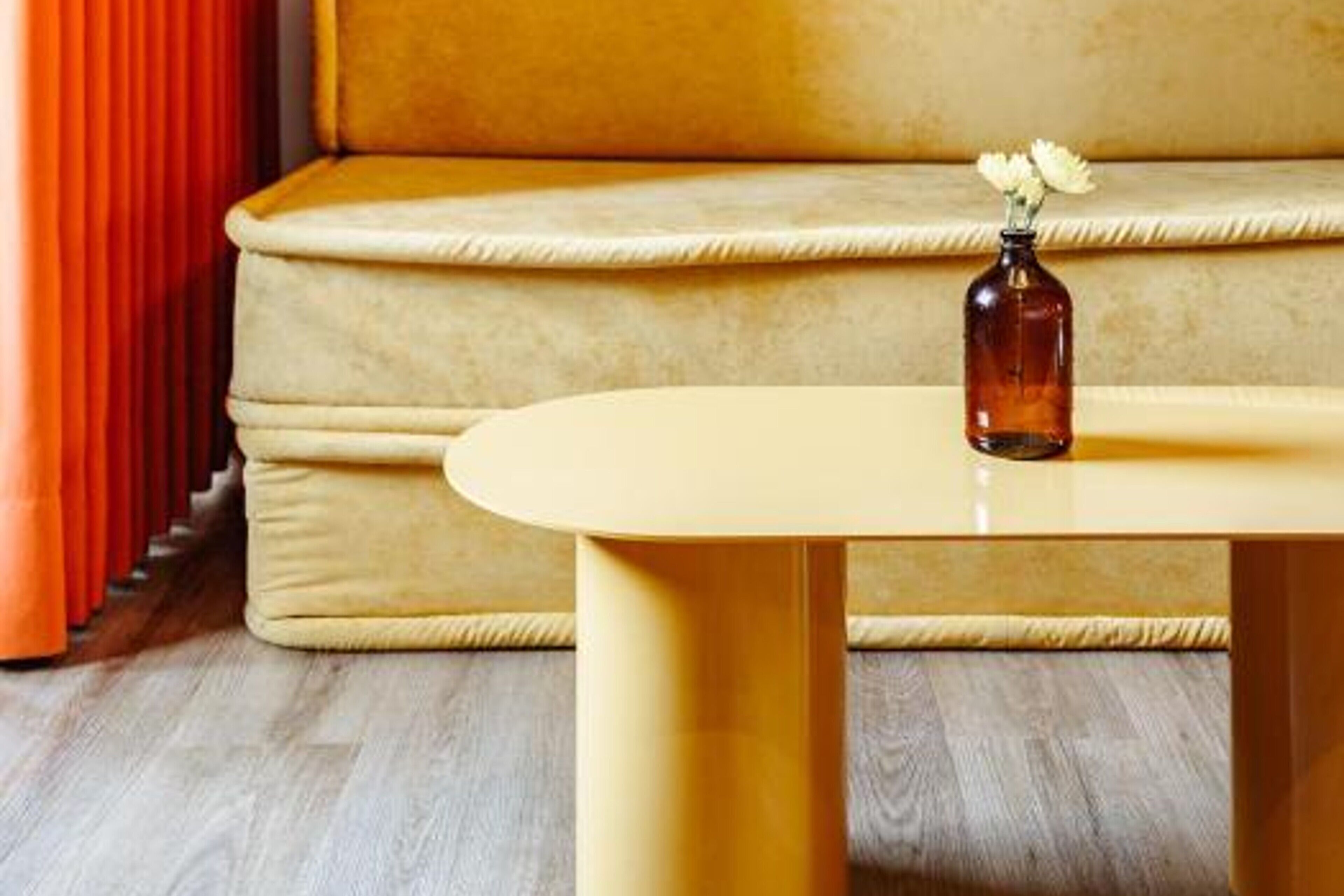A beige sofa with a vase of white flowers on a yellow table.