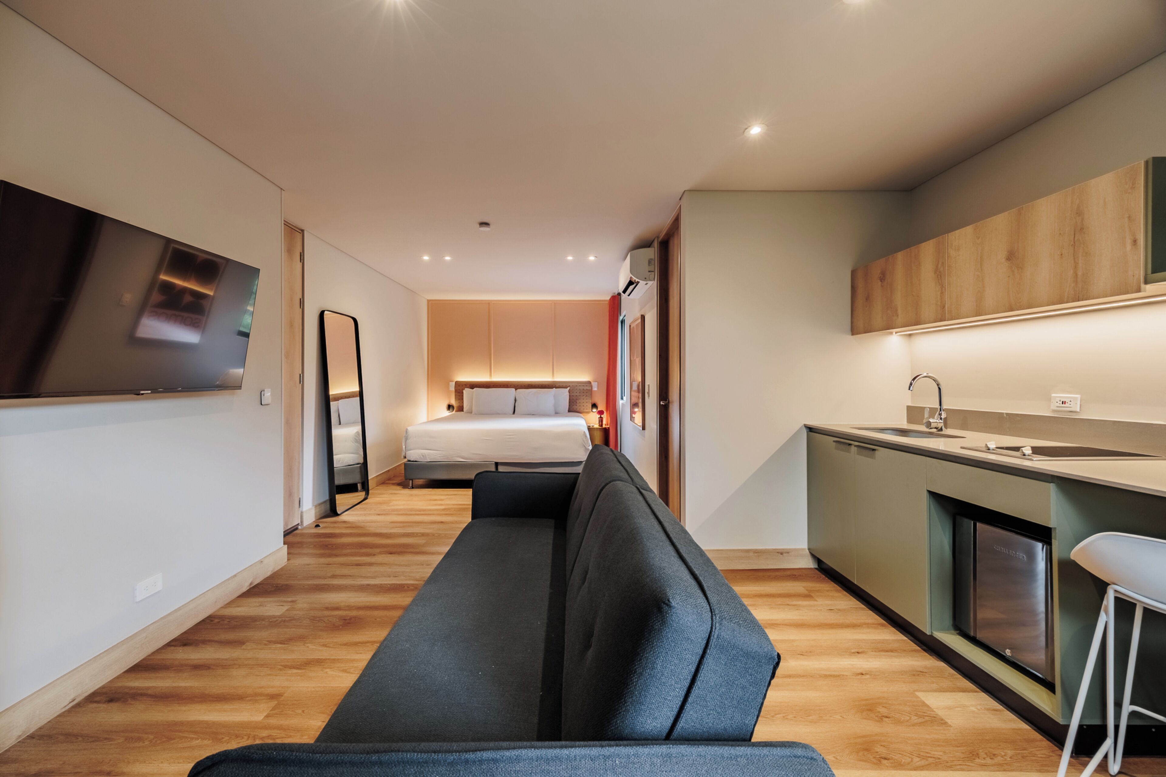Een moderne hotelkamer met een bank, een bed, een televisie, een kitchenette en een badkamer.