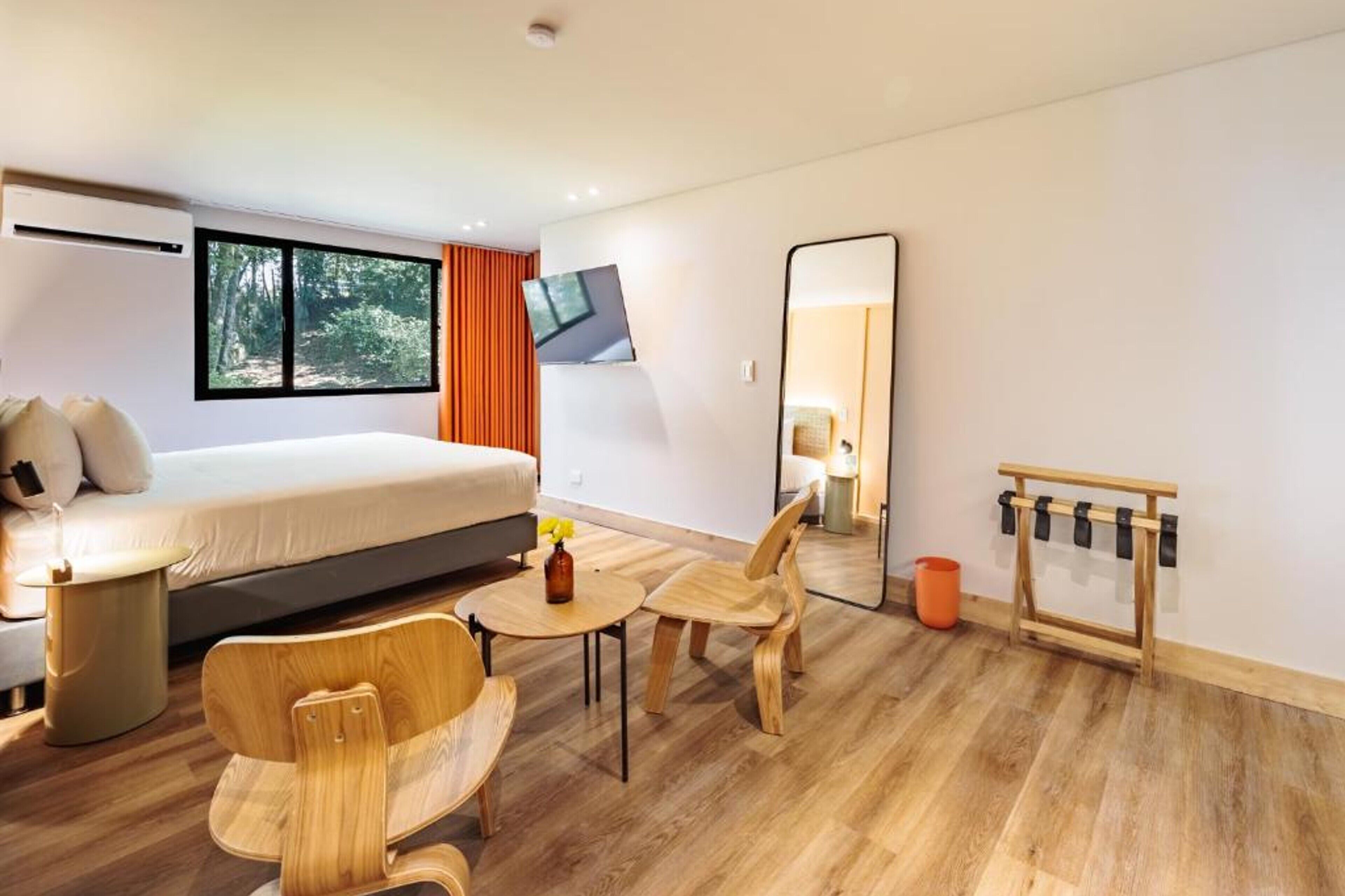 A modern hotel room with a large bed, a TV, a mirror, and wooden furniture.