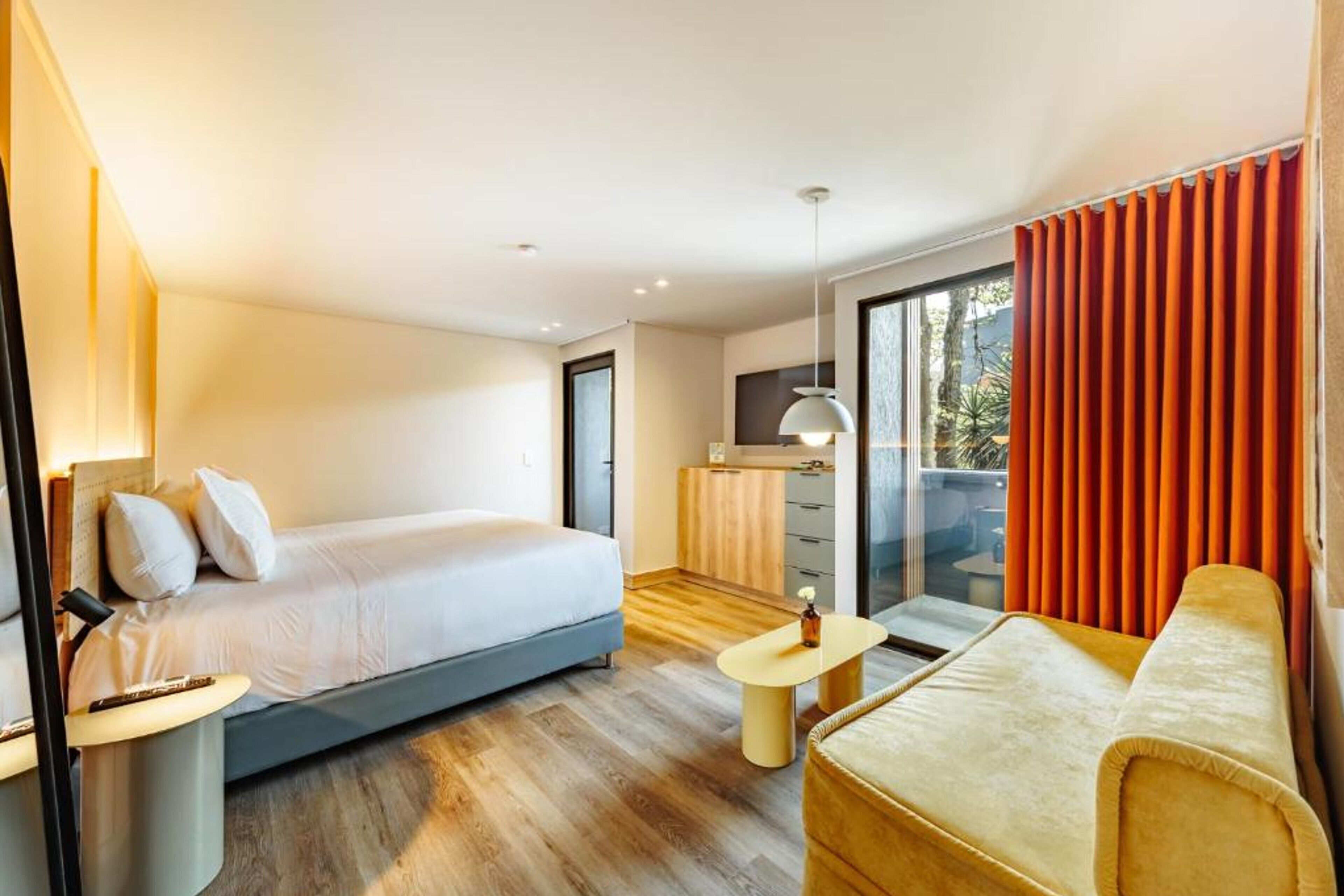 Una habitación de hotel moderna con cama, sofá, una mesita y una zona de cocina.