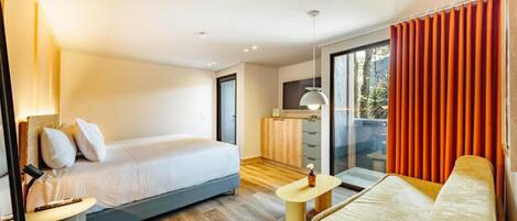 Una habitación de hotel moderna con cama, sofá, una mesita y una zona de cocina.