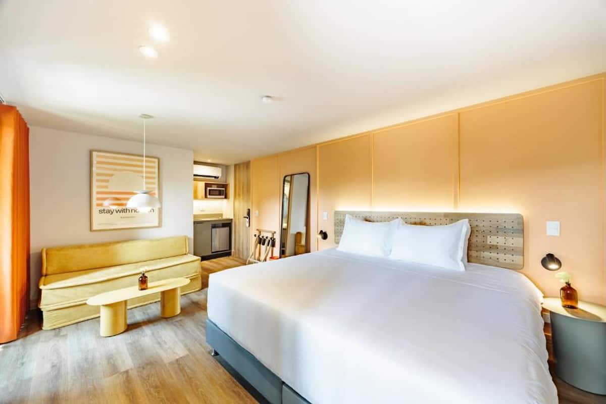 A hotel room with a large bed, a bench, a desk, a mirror, and a wall-mounted TV.