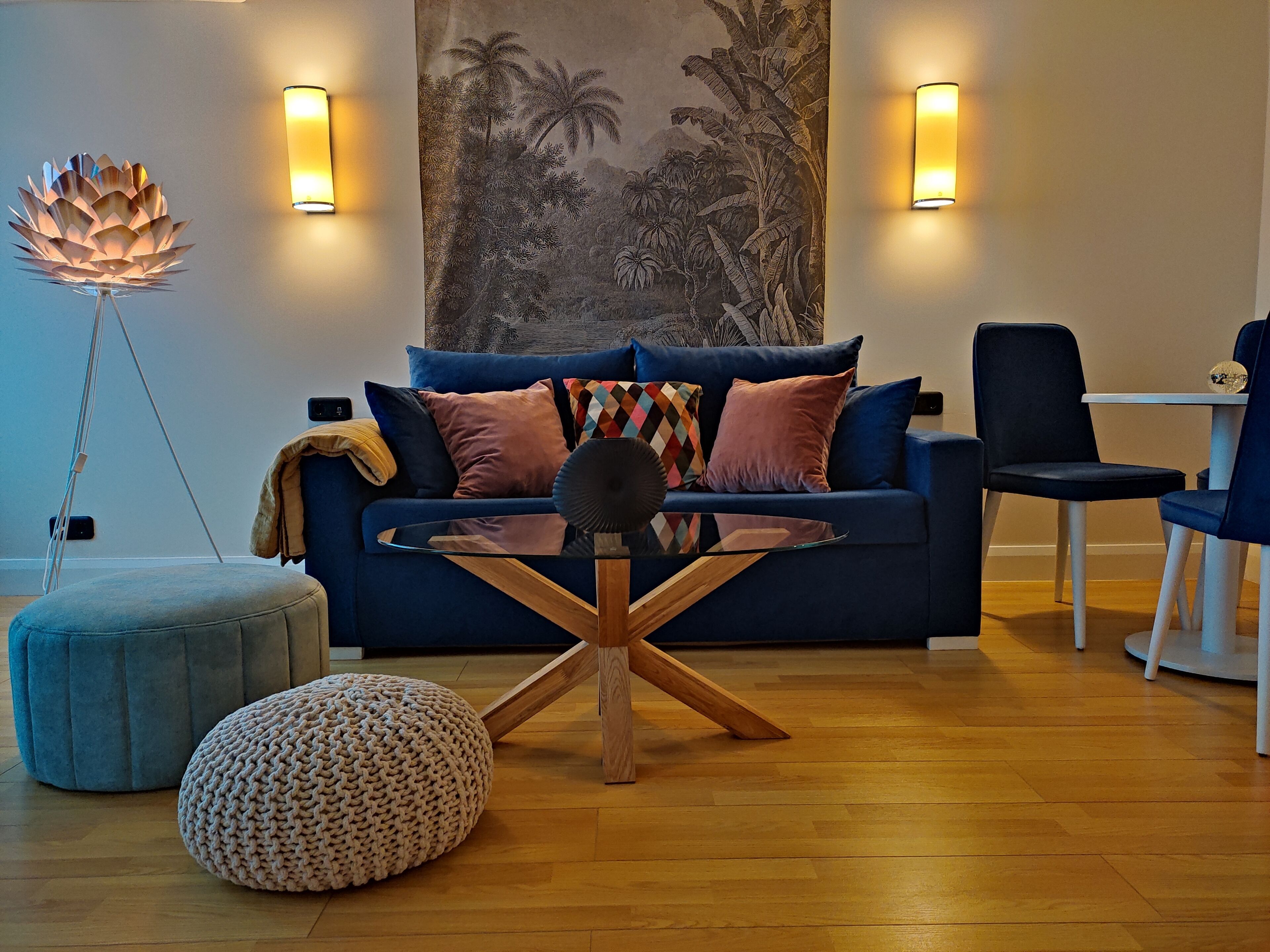 A modern living room with a blue sofa, a glass coffee table, and wooden flooring.