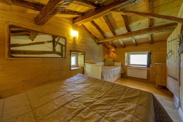 A cozy attic bedroom with a wooden ceiling, a large bed, a window, and a small bedside table. - Gîte L'Échappée en Vercors (Choranche)