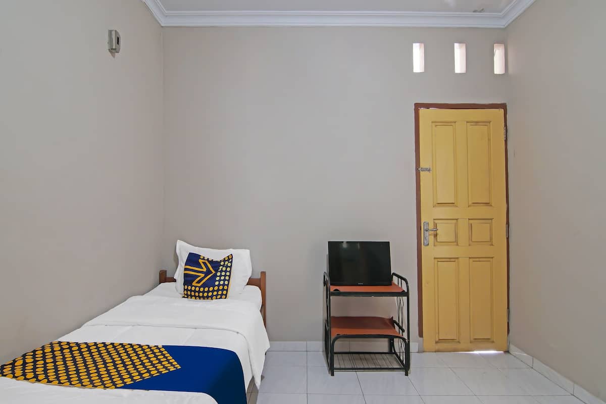 Une chambre à coucher avec un lit, un téléviseur posé sur un meuble et une porte.