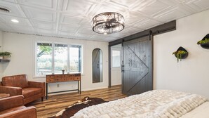 Un dormitorio con una cama grande, un sillón de cuero, un aparador de madera, un tapiz de piel de vaca y una puerta corredera de estilo granero.