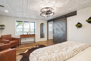 A bedroom with a large bed, a leather armchair, a wooden dresser, a cowhide rug, and a sliding barn-style door. - The Lodge at Shaw Ranch | Hocking Hills, 30 Acres (Rockbridge)