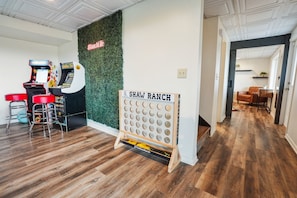 Ein Zimmer mit Holzboden, einer Wand mit grünem Blättermotiv, einem Schild mit der Aufschrift 'SHAW RANCH' und einer Dartscheibe.