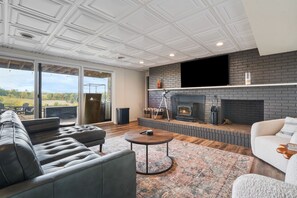 A modern living room with a fireplace, leather sofas, and a large window overlooking a scenic view.