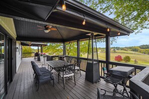 A covered outdoor deck with a table and chairs, a grill, and a view of the surrounding landscape. - The Lodge at Shaw Ranch | Hocking Hills, 30 Acres (Rockbridge)