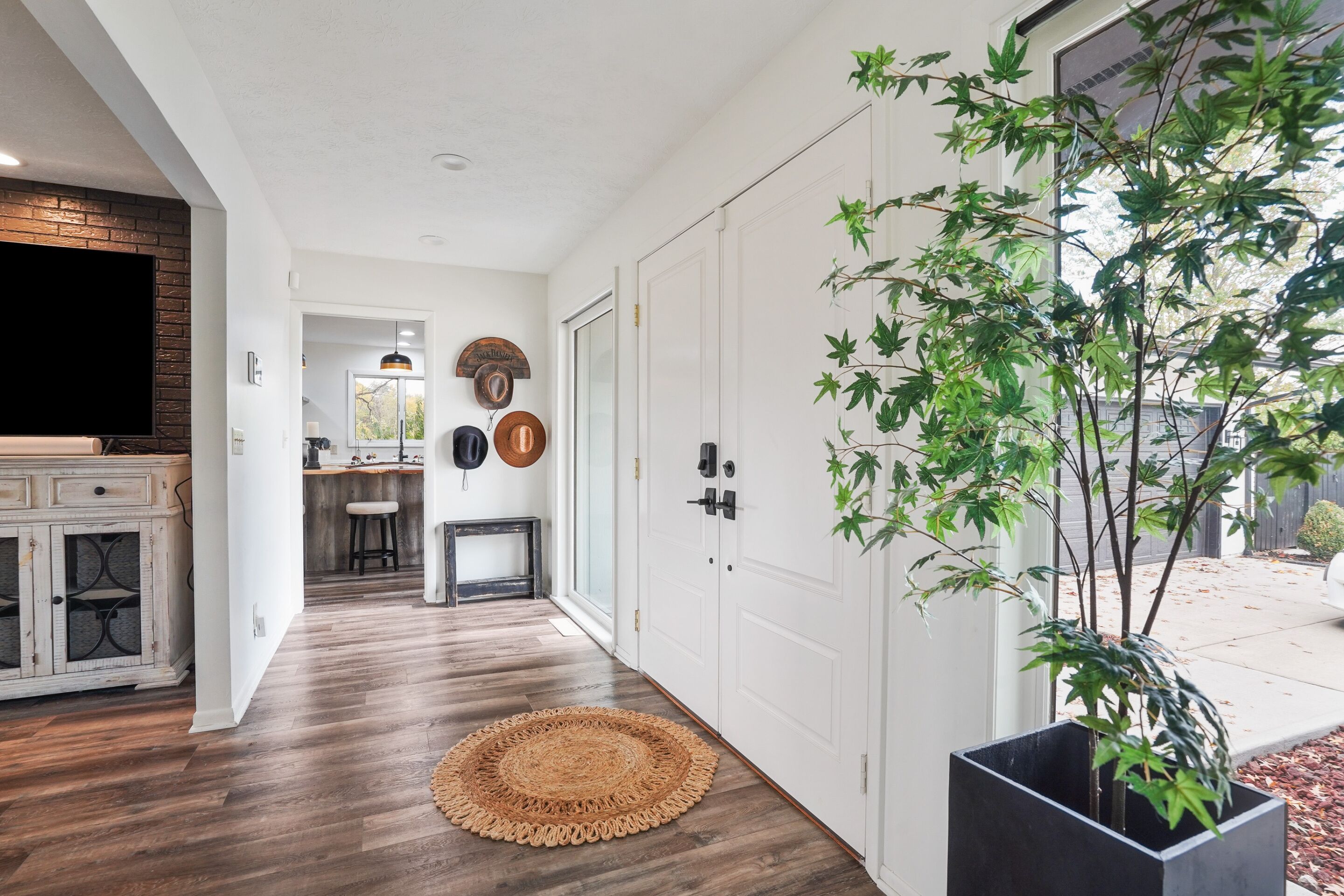 A hallway with a wooden floor, a round woven rug, a potted plant, and a door with a coat of arms.