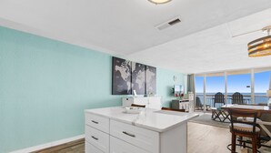 A modern kitchen with white cabinetry, a marble countertop, and a world map artwork on the wall. - Garden City Beach Oceanfront Condo 1108 | Rising Tides Properties Rental (Murrells Inlet)